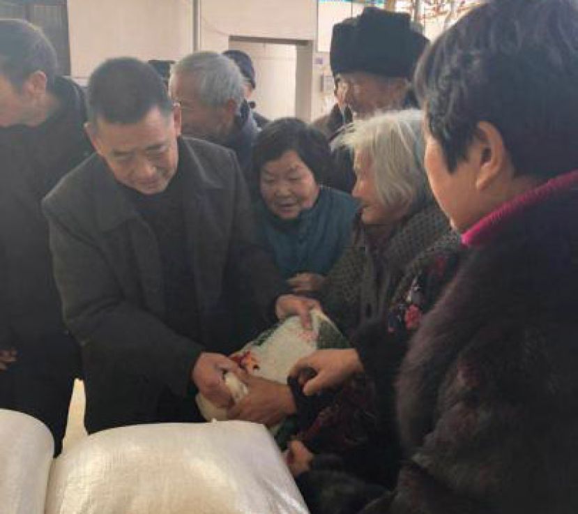 图示：陆润德在现场亲手将大米一袋一袋地分到现场数百名老人手中。