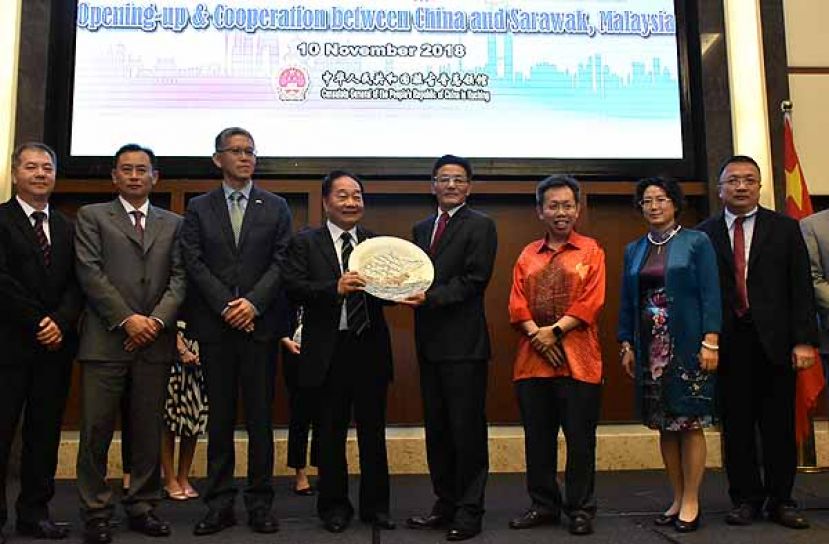 图示：中国驻古晋总领事程广中（右四）赠送纪念品予首席部长，由砂国际贸易与电子商务部部长拿督斯里黄顺舸（左四）代领。