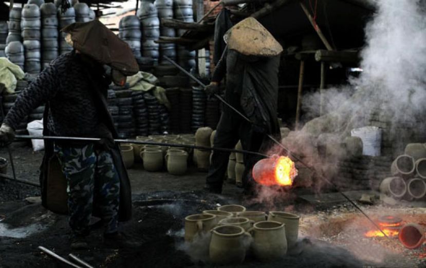 图示：两位工人师傅将刚烧制出的荥经砂器挑入坑中。