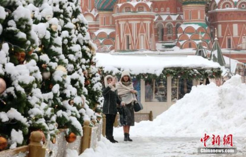 资料图：两名俄罗斯民众站在白雪覆盖的红场上，其中一人用手机拍摄雪景。