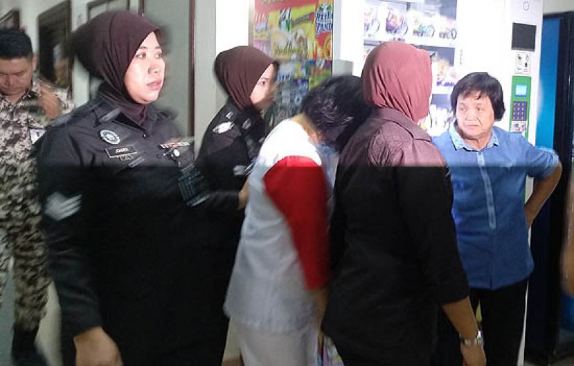 双手铐着手铐的林咸慈藏在狱卒身后并垂下头经过正在哈腰的家婆时摄。