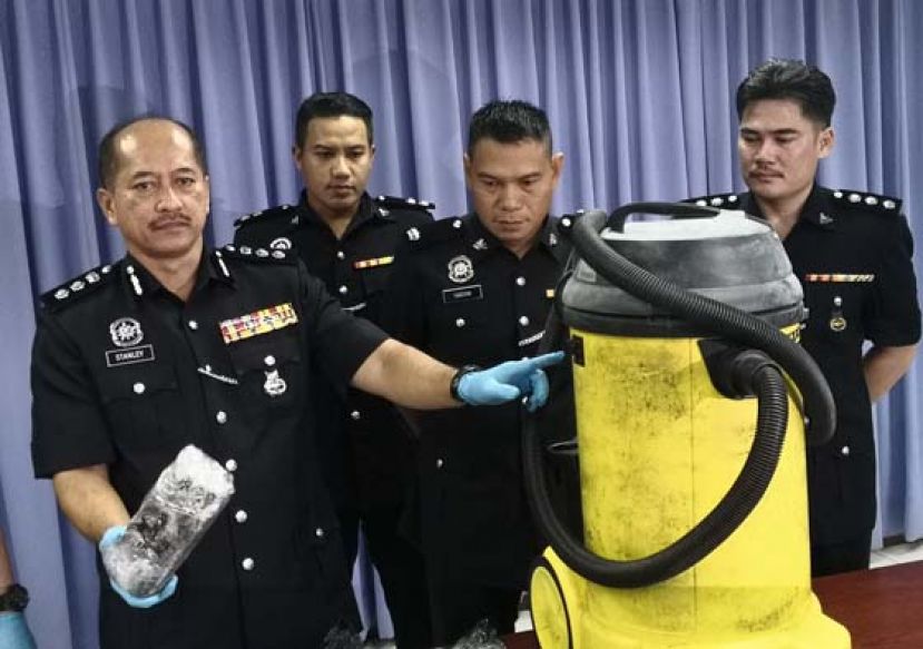 诗巫警区主任史丹利助理总监（左一）向媒体讲述警方在这个黄色的吸尘机桶里发现了大麻。