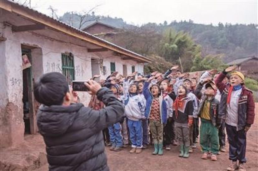 图示：孩子们参加升旗仪式，李华用手机记录下孩子们专注的神情。