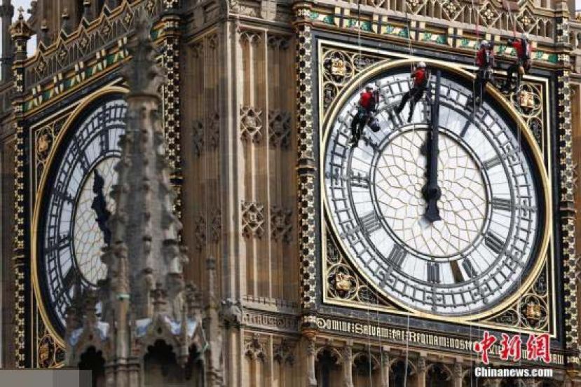 资料图：英国伦敦，工作人员吊在大本钟的钟面上进行清洁工作。
