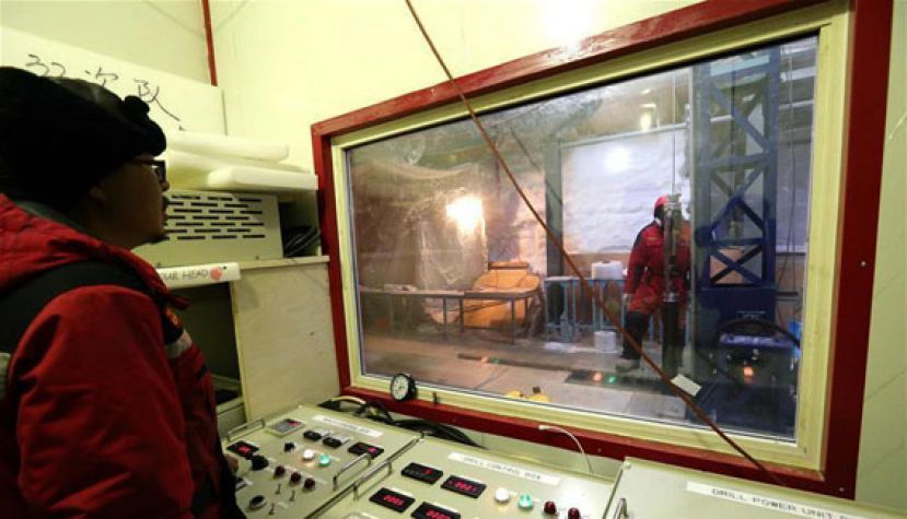 图示：科考队员范晓鹏（左）在控制室内操作控制器，将钻机缓缓送入钻探导向孔。